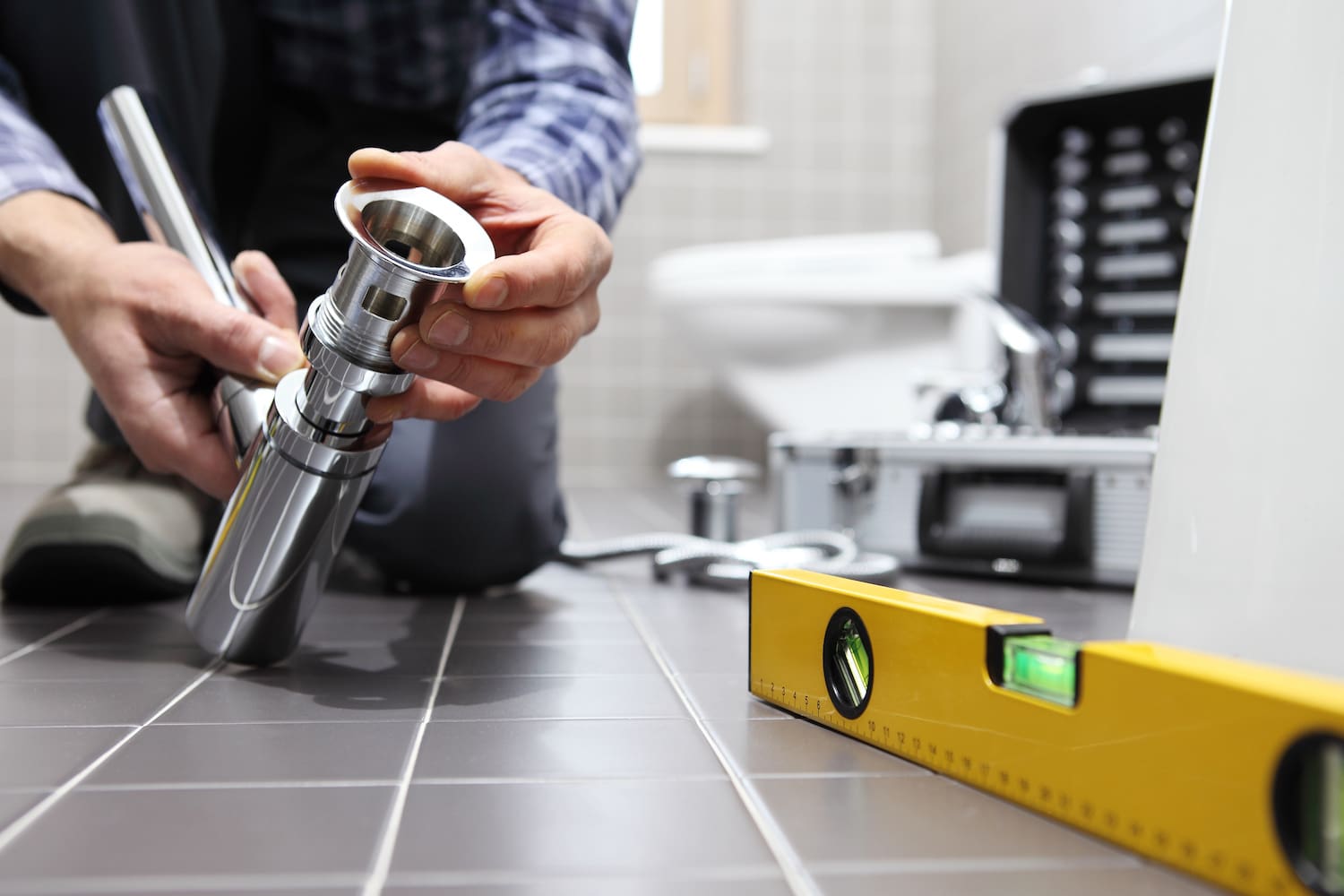 budget small bathroom remodel closeup of man's hands working with bathroom plumbing and tools with level in the foreground