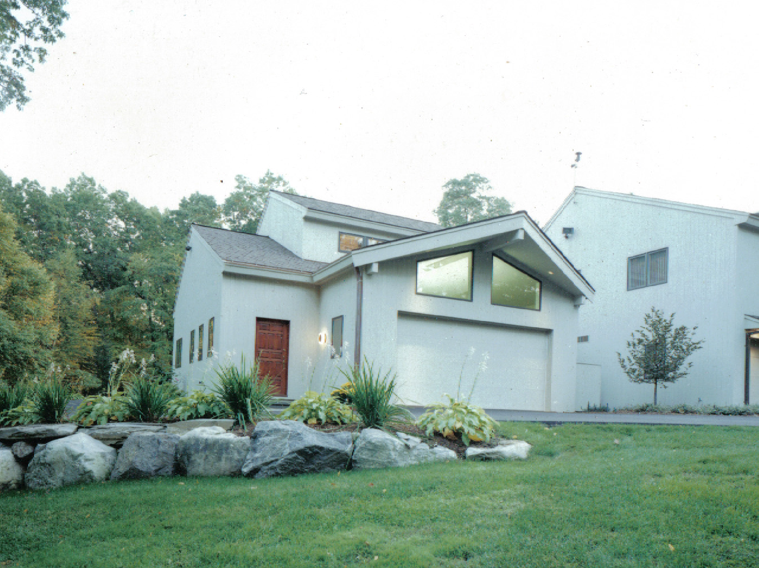 Modern white house with a unique geometric design, featuring large windows and surrounded by lush greenery and a stone garden border.